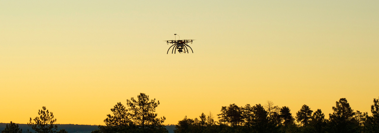 A drone flying over the treeline during sunset